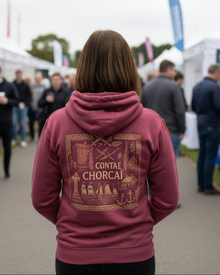 Person wearing a maroon hoodie with gold design and text at an outdoor event.