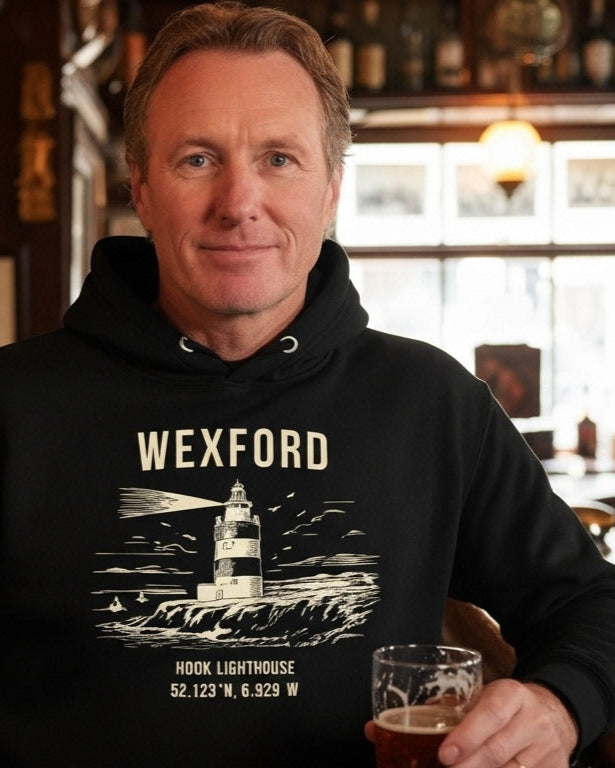 Man wearing a black hoodie with 'Wexford' design, holding a glass in a bar setting.