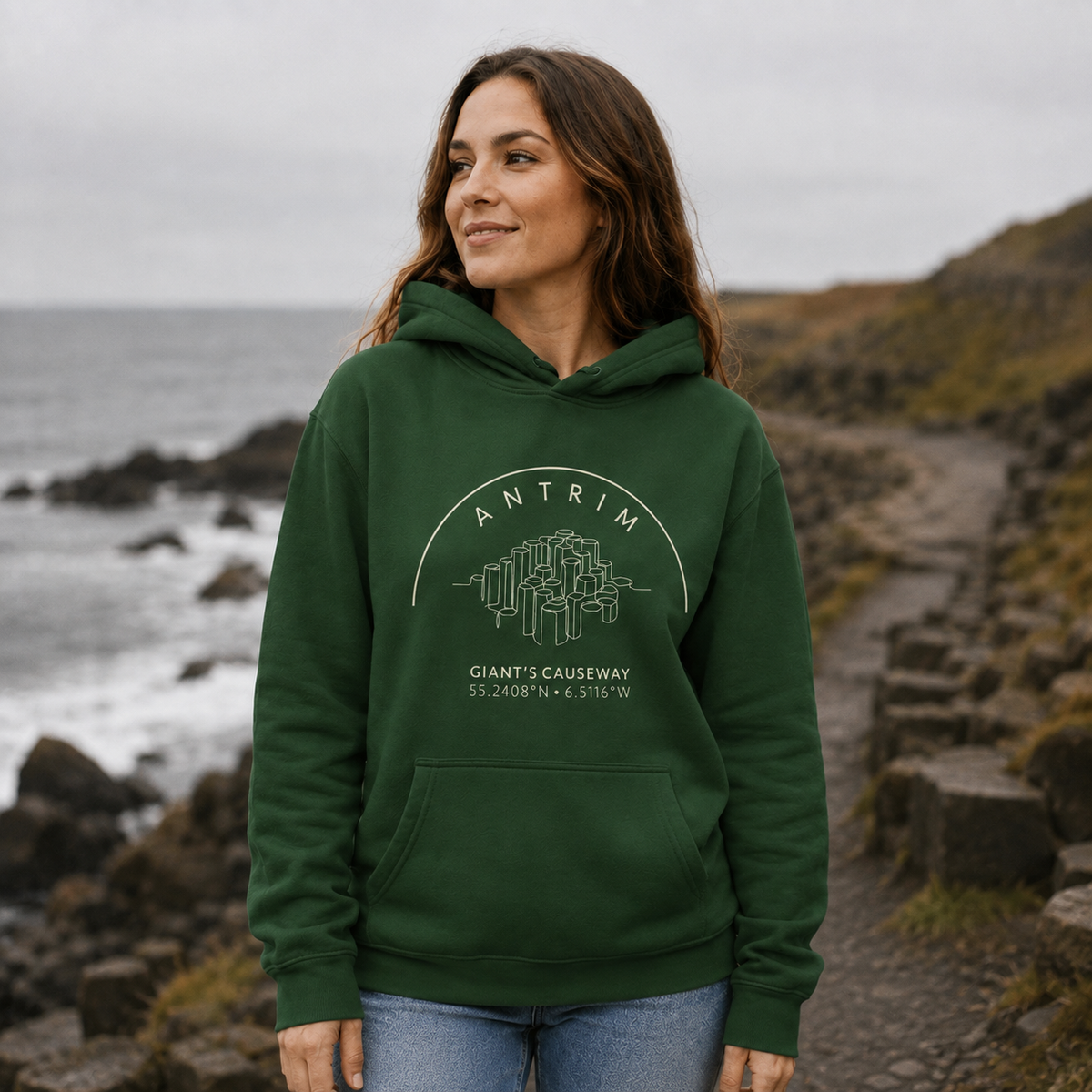 Woman wearing the Antrim Giant’s Causeway forest green hoodie on the Antrim coast