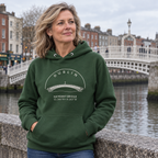 Woman wearing the Dublin Ha’penny Bridge forest green hoodie beside the River Liffey
