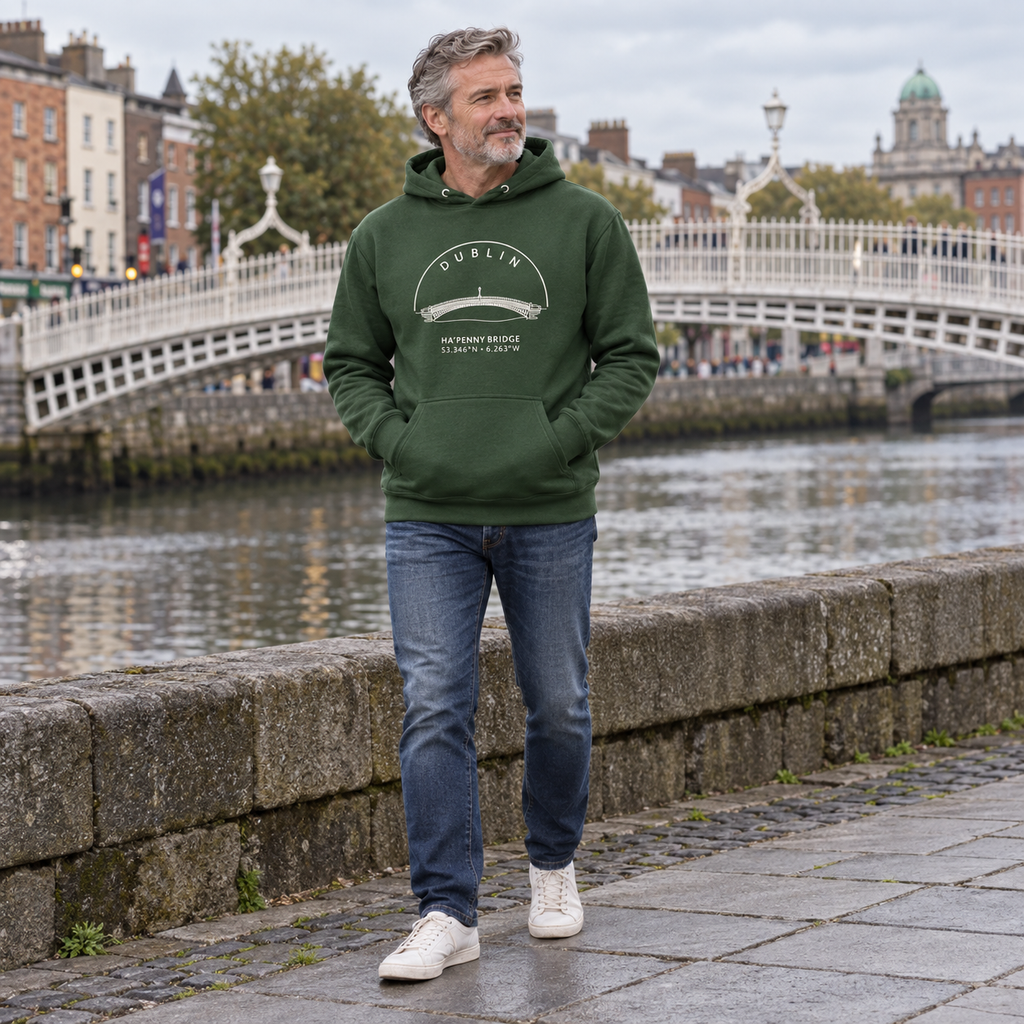 Man wearing the Dublin Ha’penny Bridge forest green hoodie beside the River Liffey